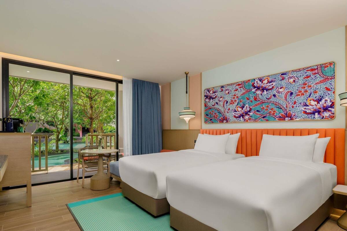 A hotel room with two beds, a dining area, and a view of a pool.