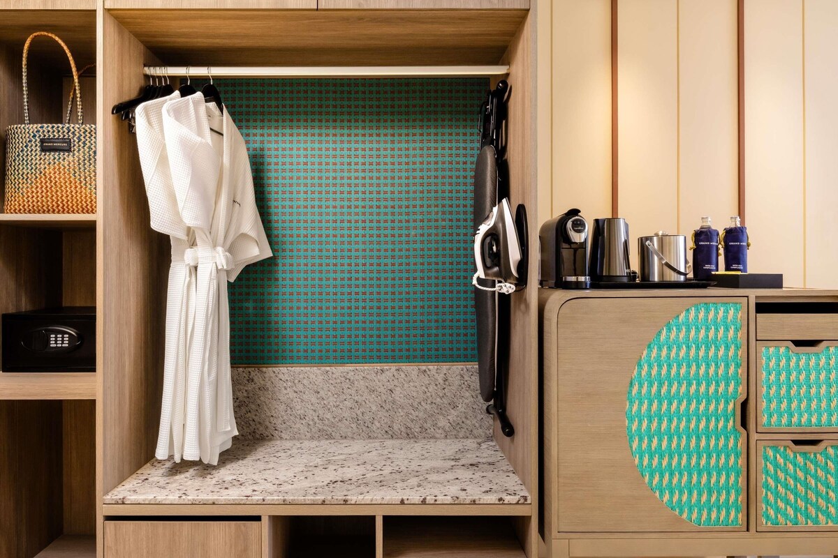 Een compacte hotelkamer met een kitchenette, een badjas, een paar slippers en een gestreept kastje.