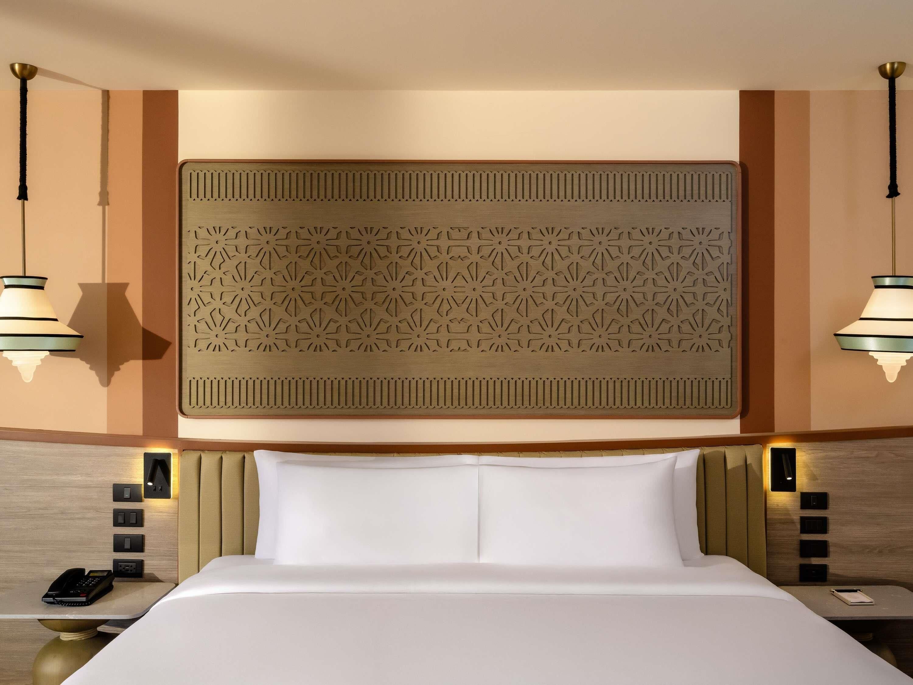 A hotel room with a large bed, a decorative wall panel, bedside lamps, and a bedside phone.