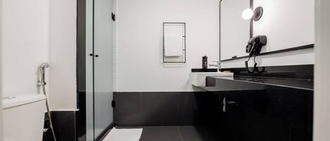A modern bathroom with a toilet, a glass shower enclosure, a sink with a mirror, and a hairdryer on the counter.