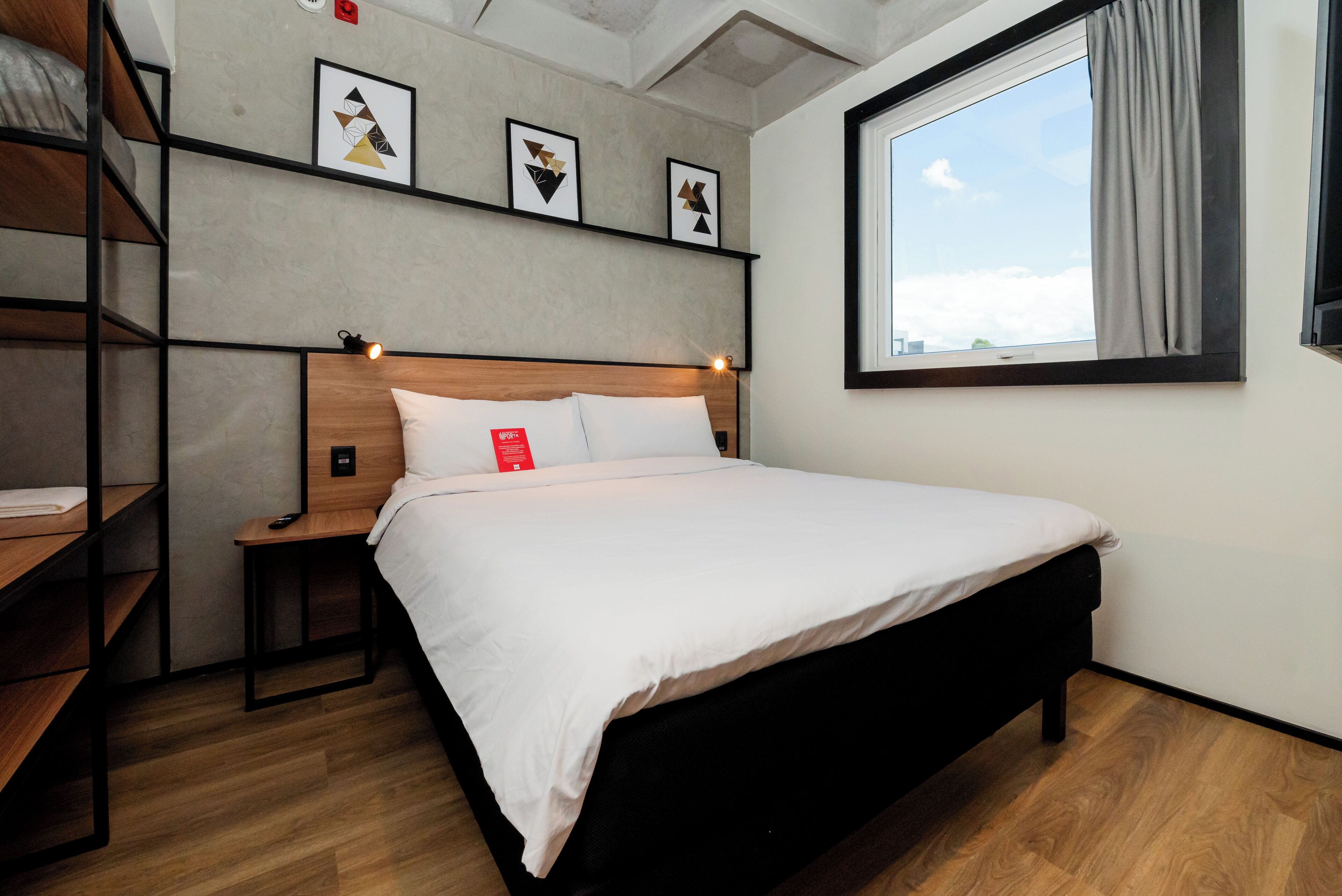 Une chambre d’hôtel moderne avec un lit en bois, une table de chevet, une étagère avec des œuvres d’art et une fenêtre avec des rideaux.