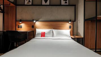 A hotel room with a wooden headboard, a bed with white linens, a desk with a chair, and framed artwork on the wall.