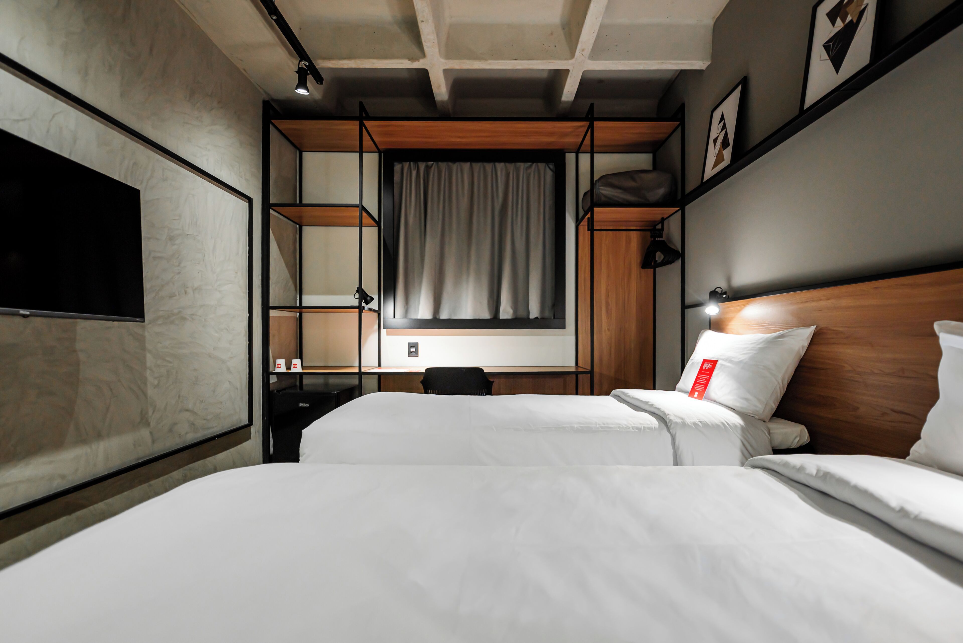 A hotel room with a large bed, a desk, a chair, a TV, and a window with curtains.