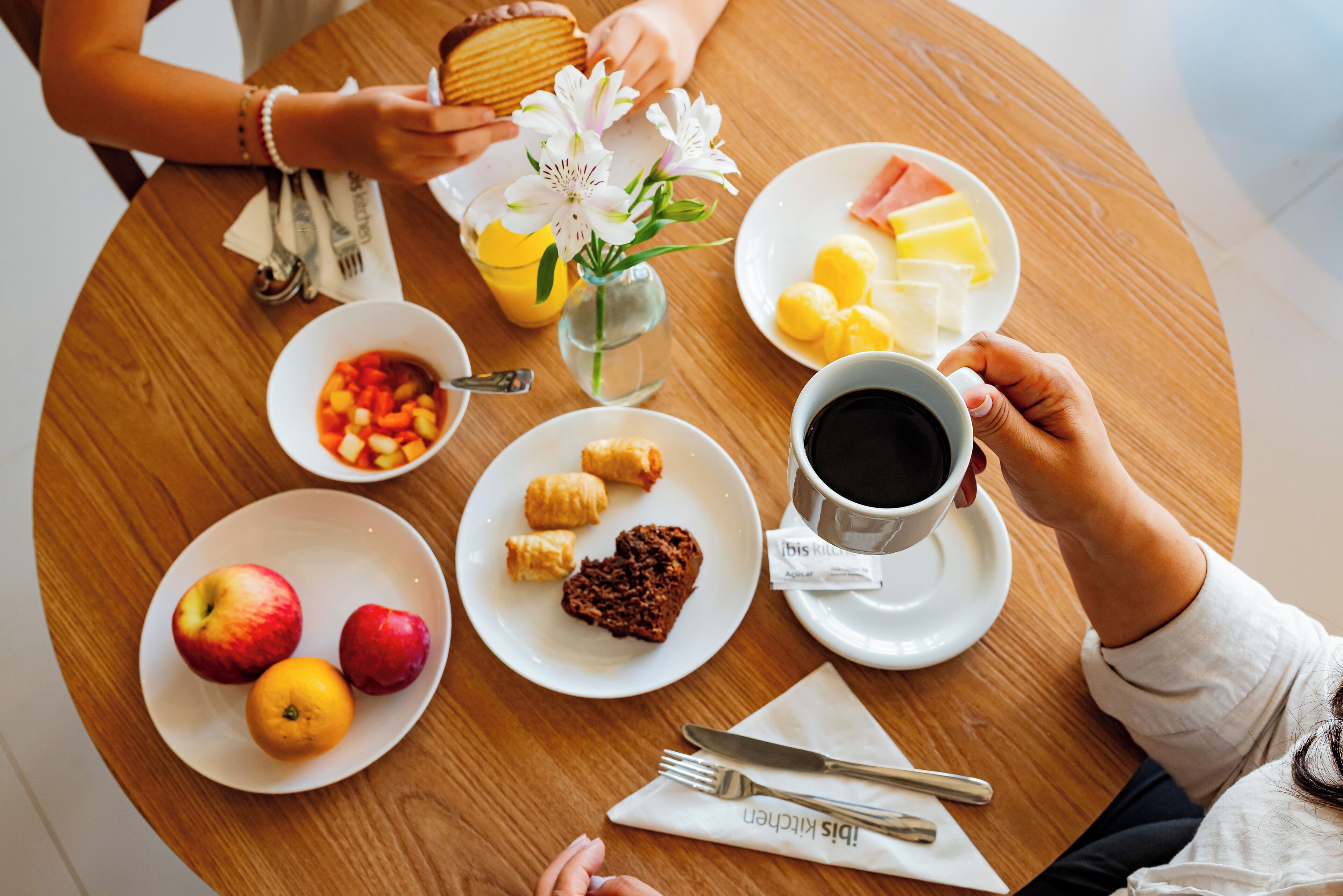 A round wooden table with breakfast items including fruits, pastries, and coffee.