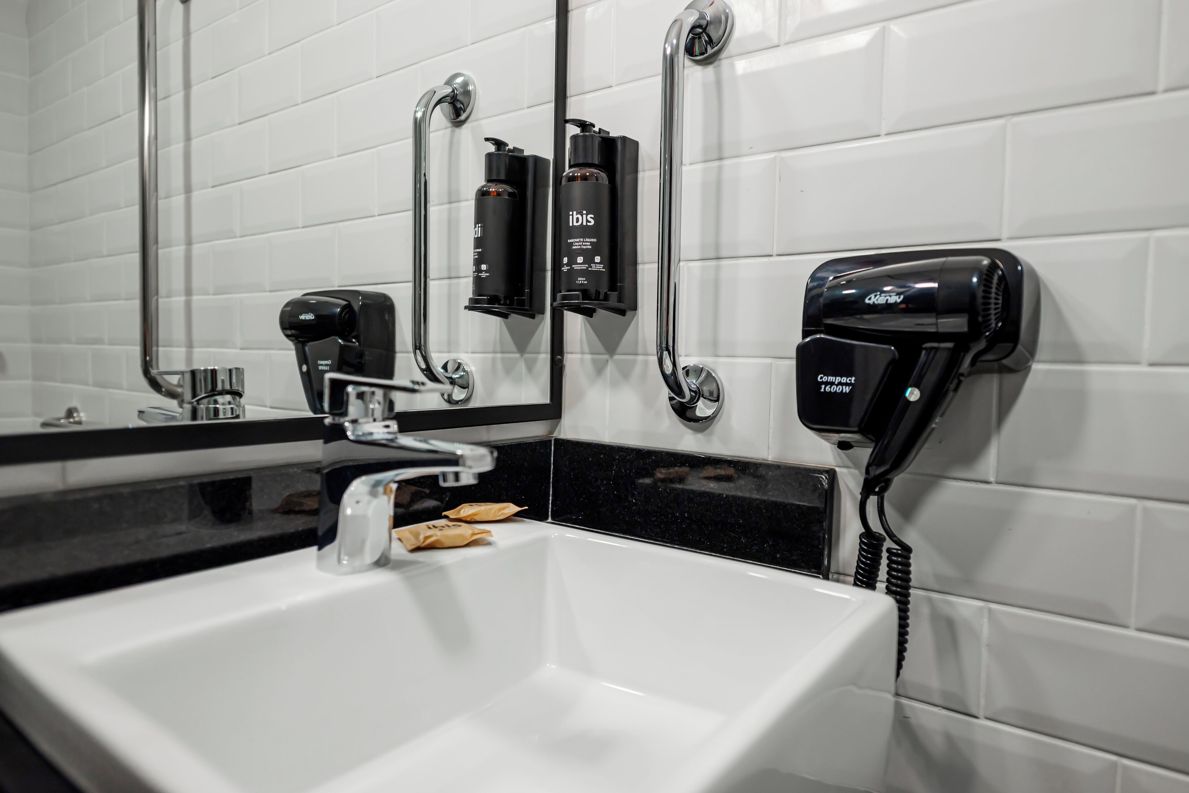 Baño con lavamanos blanco, espejo y secador de pelo montado en la pared.