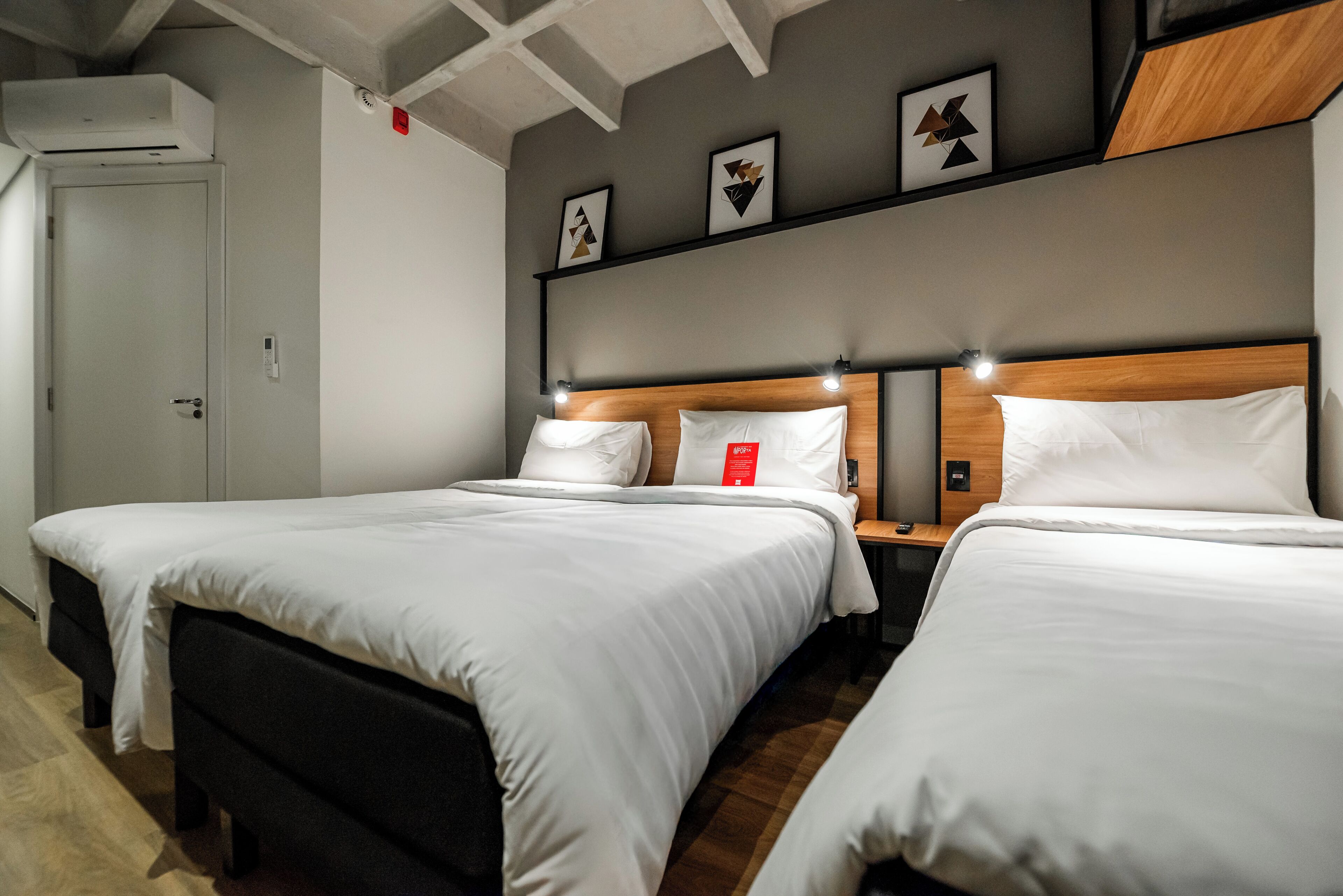 Habitación de hotel con dos camas, cabecero de madera, mesita de noche y lámpara de pared.