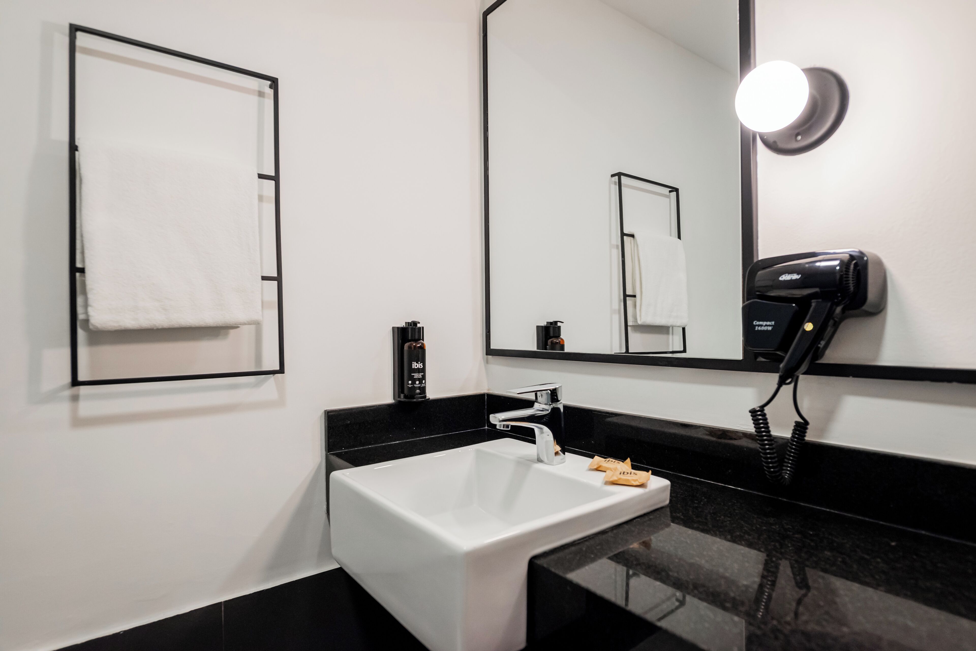 A modern bathroom with a white sink, black countertop, and a hairdryer on the wall.