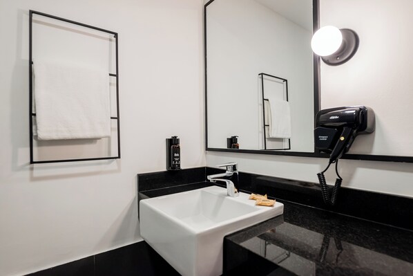 Ein modernes Badezimmer mit einem weißen Waschbecken, einer schwarzen Arbeitsplatte und einem an der Wand befestigten Föhn.