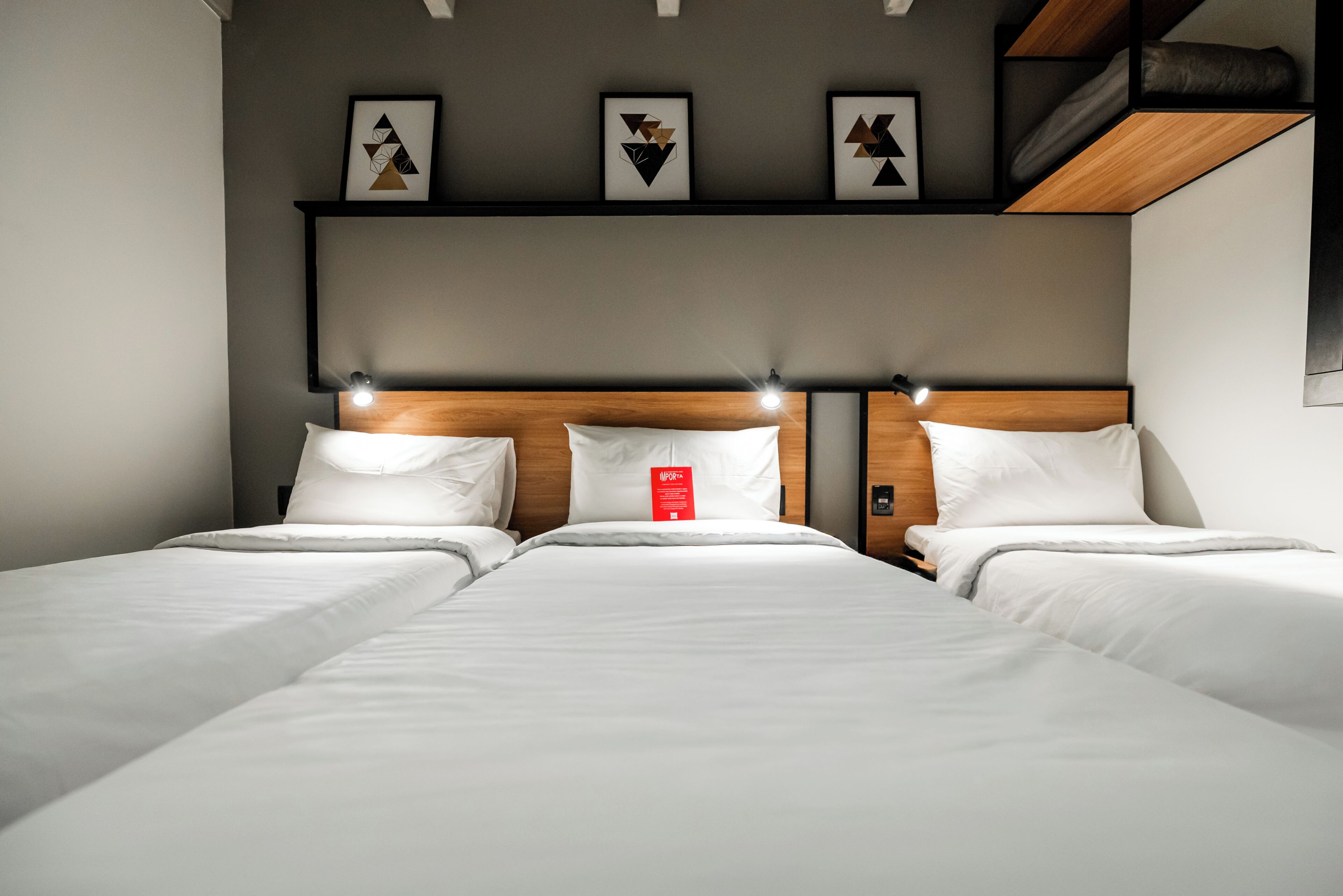 Una habitación de hotel con una cama grande, un cabecero con iluminación integrada y tres cuadros geométricos enmarcados.
