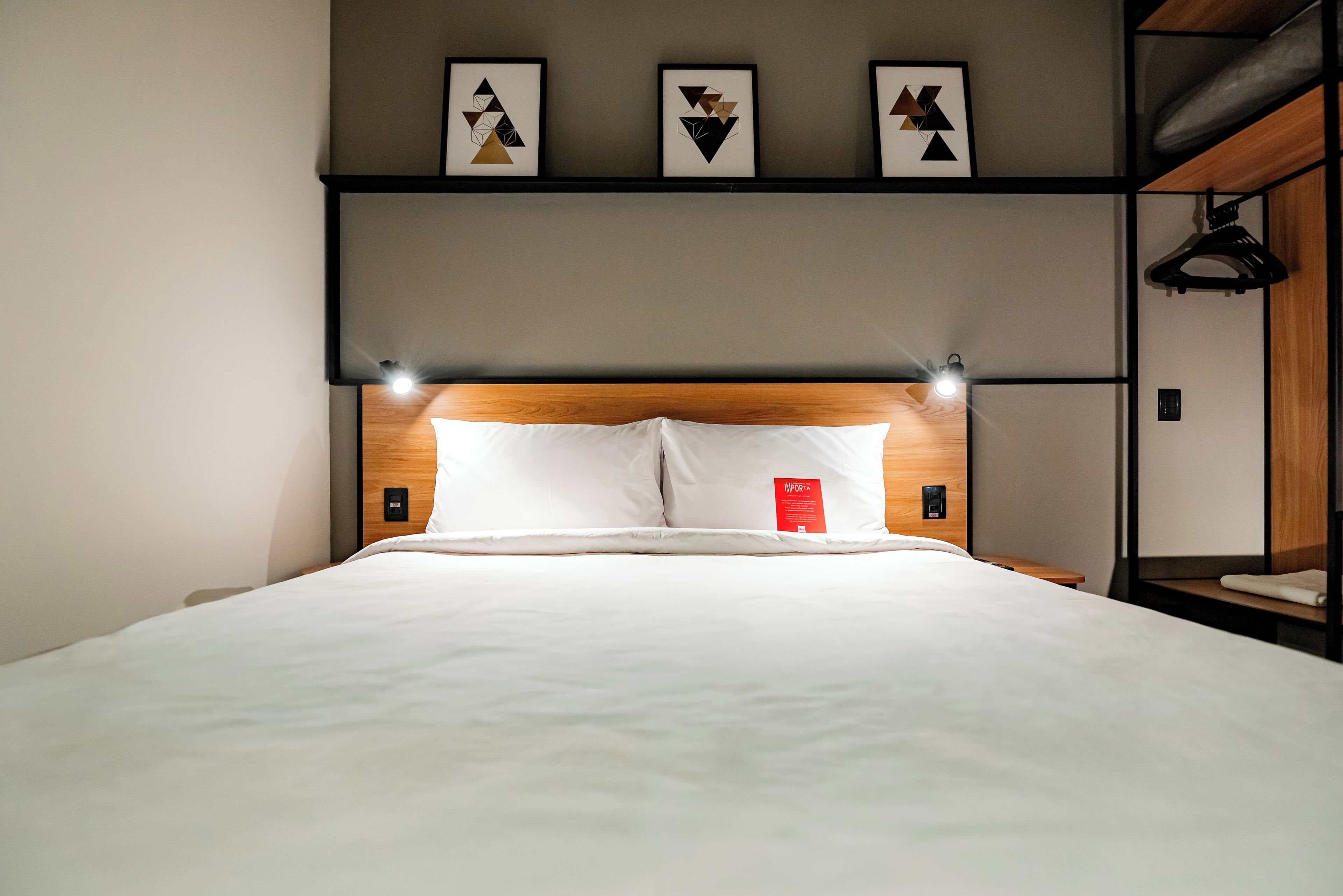 A neatly made bed with white linens, a wooden headboard, and three wall-mounted picture frames above it.