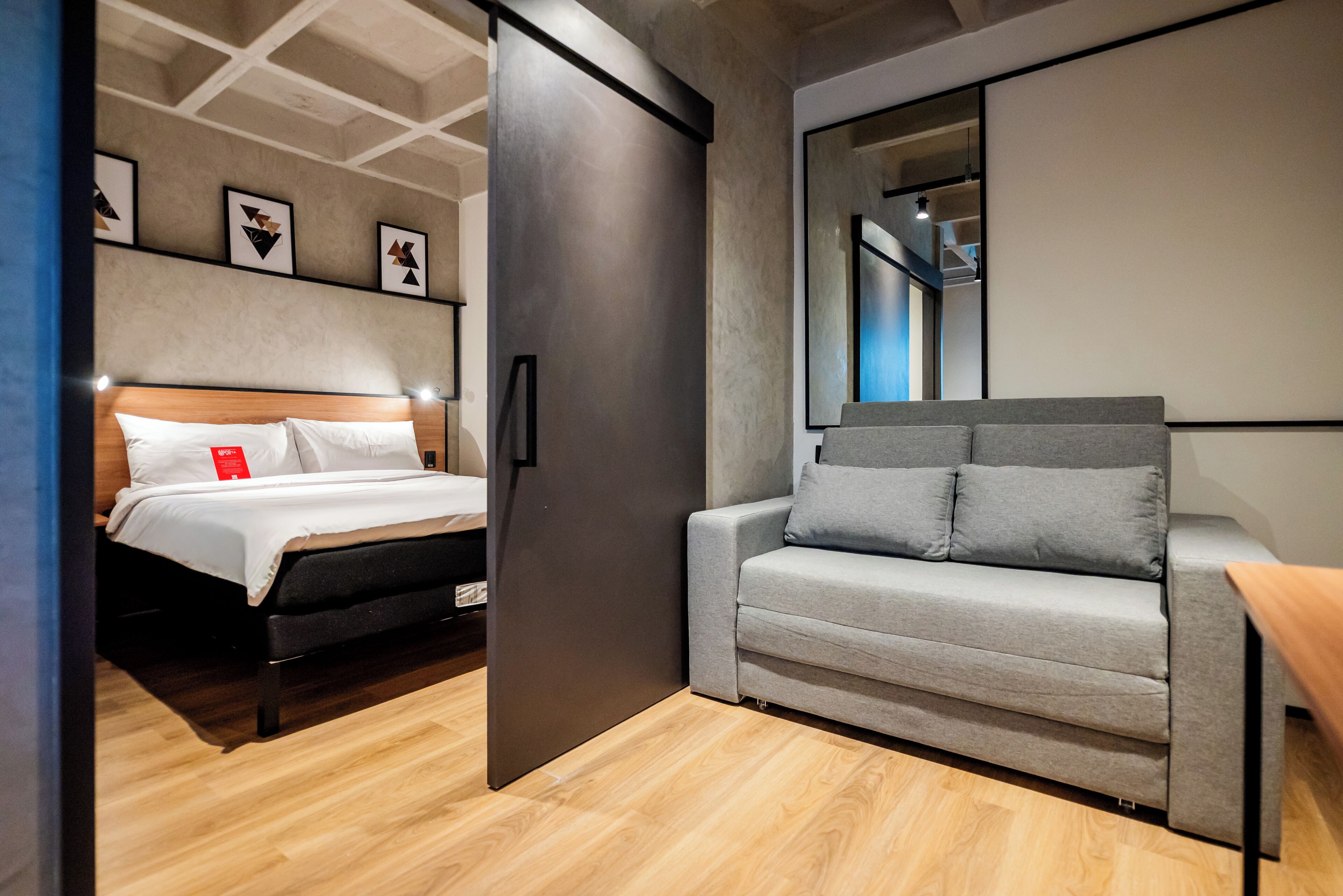 Ett modernt hotellrum med en säng, en soffa, en stor spegel och konstverk på väggen.