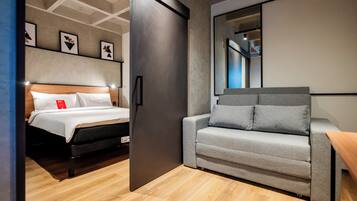 Ett modernt hotellrum med en säng, en soffa, en stor spegel och konstverk på väggen.