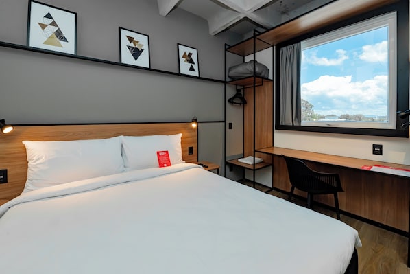 A hotel room with a bed, a desk, and a window with a view. - ibis Pelotas (Pelotas)