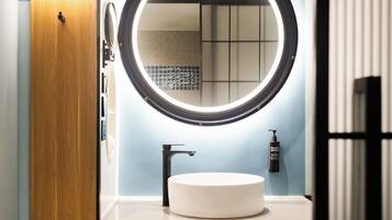 A bathroom with a round mirror, a white sink, and a wooden door.