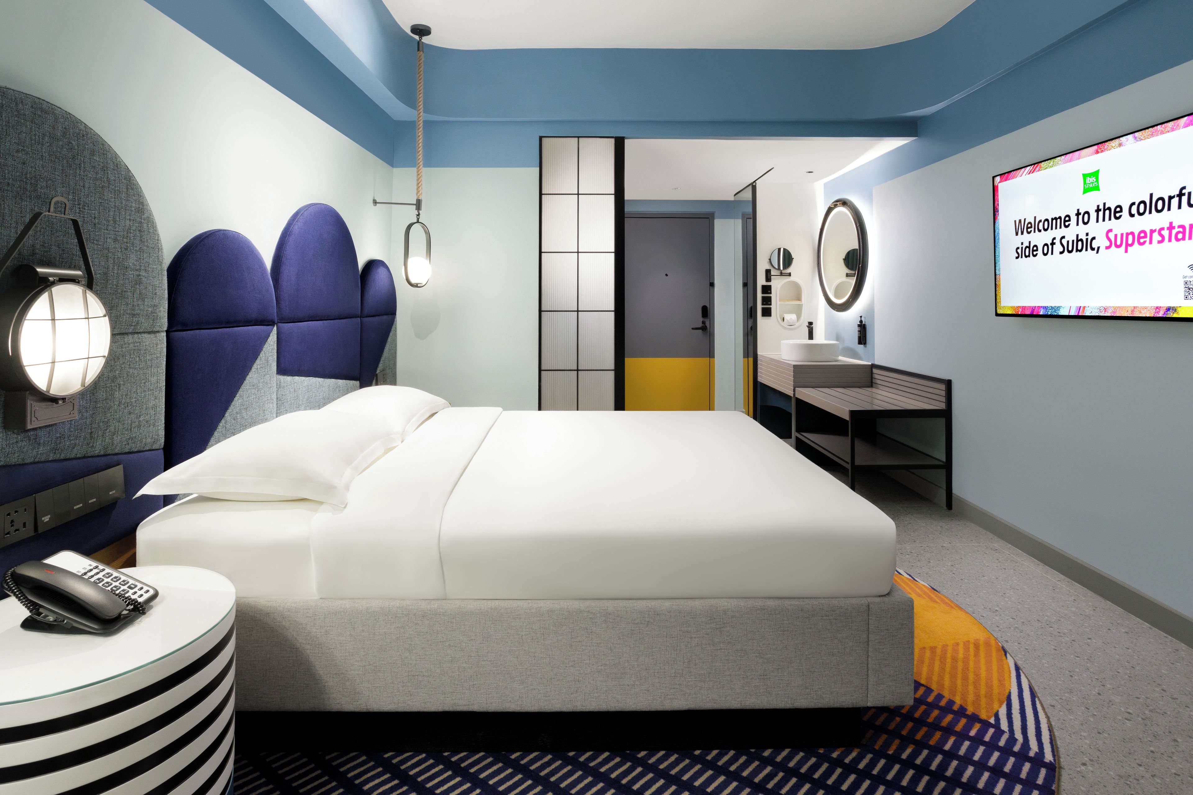 A modern hotel room with a bed, bedside table, and a TV screen displaying a welcome message.