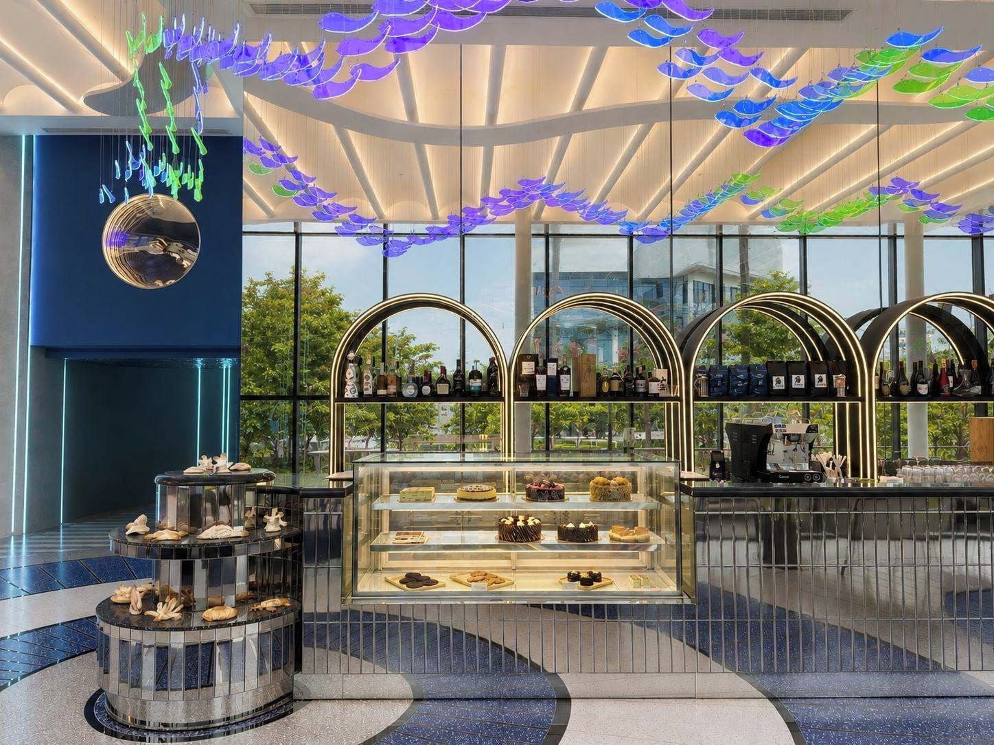 A modern interior with a glass display case containing pastries, a coffee machine, and a selection of bottled beverages.