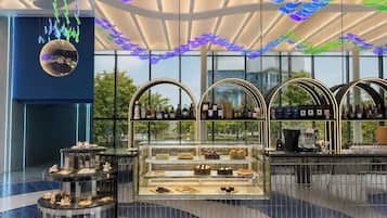 A modern interior with a glass display case containing pastries, a coffee machine, and a selection of bottled beverages.
