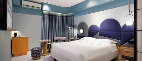 A modern hotel room with a bed, bedside table, lamp, and a view of the city.
