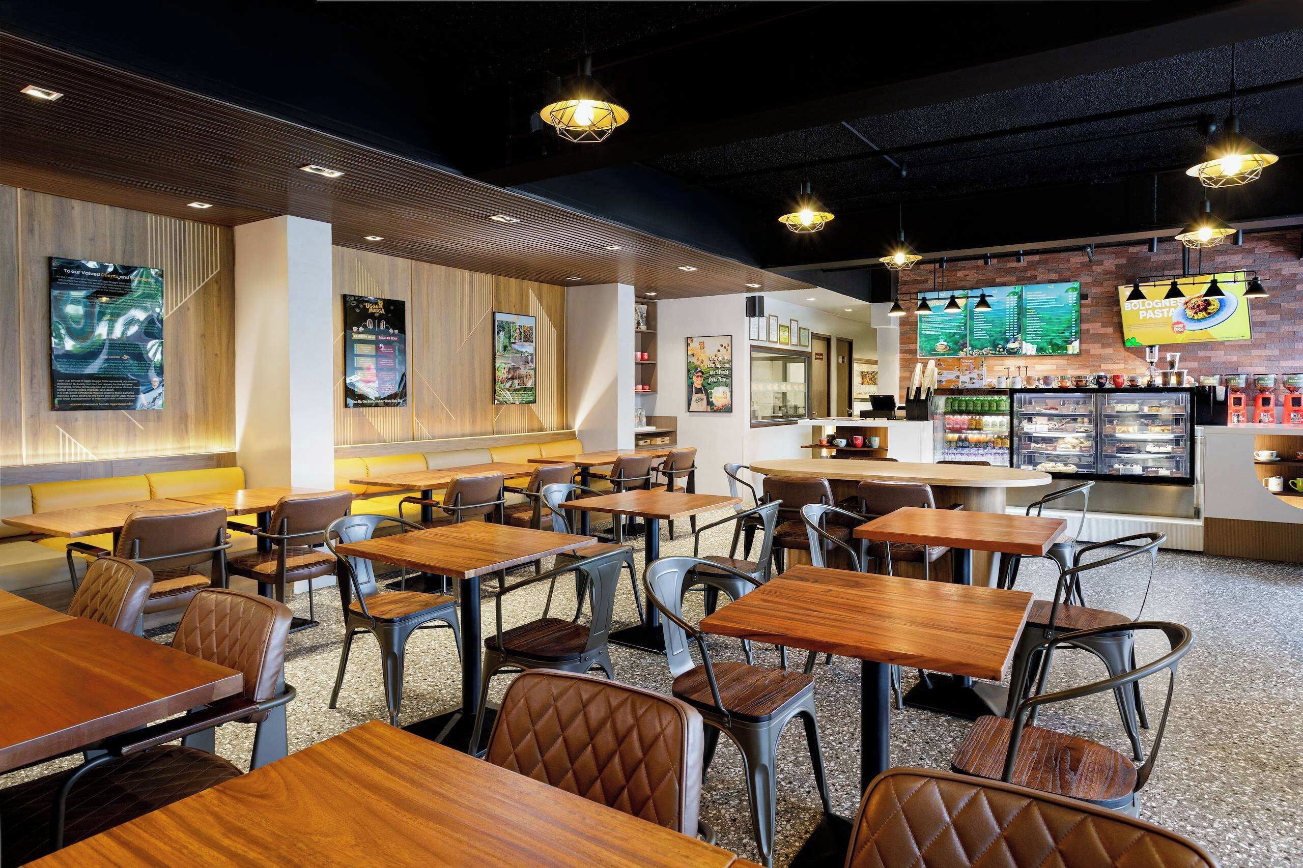 A restaurant interior with multiple tables and chairs, a counter with a menu display, and a refrigerated display case.