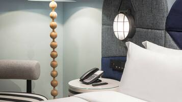 Una habitación de hotel moderna con una cama, un escritorio con teléfono, una lámpara y un aplique de pared.