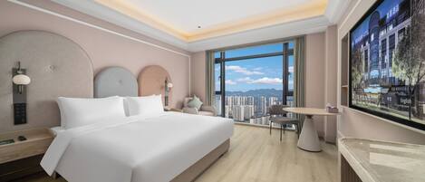 A modern hotel room with a large bed, a desk, a chair, a TV, and a view of the city.