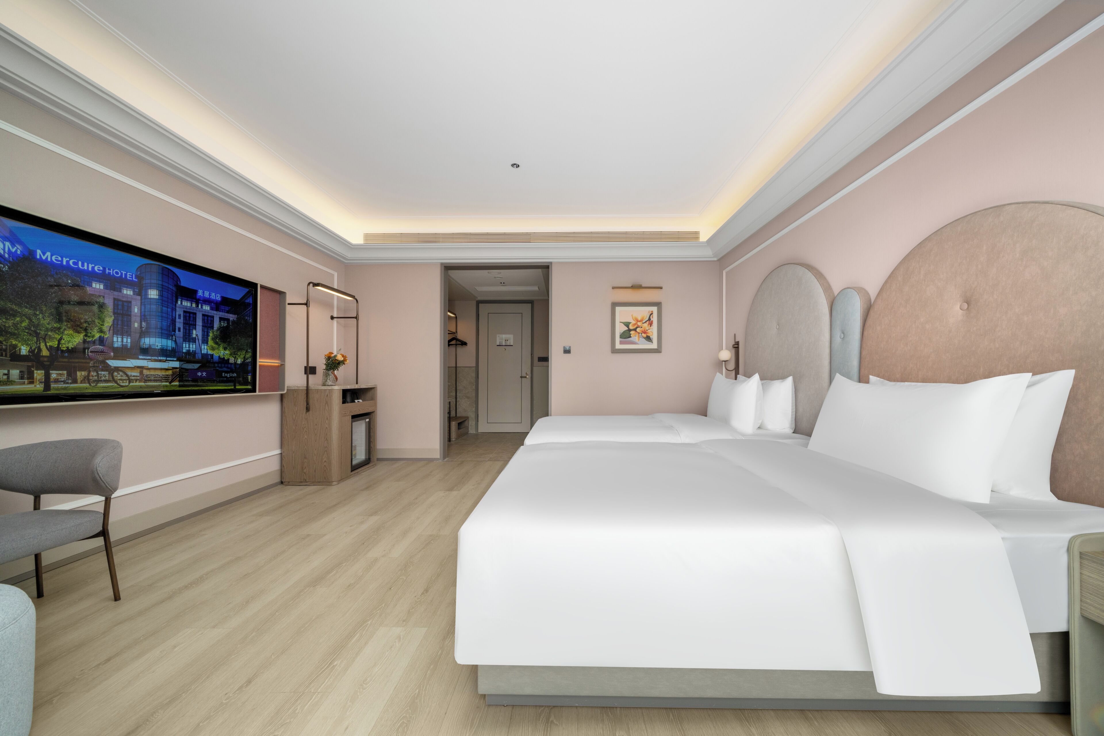 A hotel room with a large bed, a TV on the wall, a desk, and a chair.