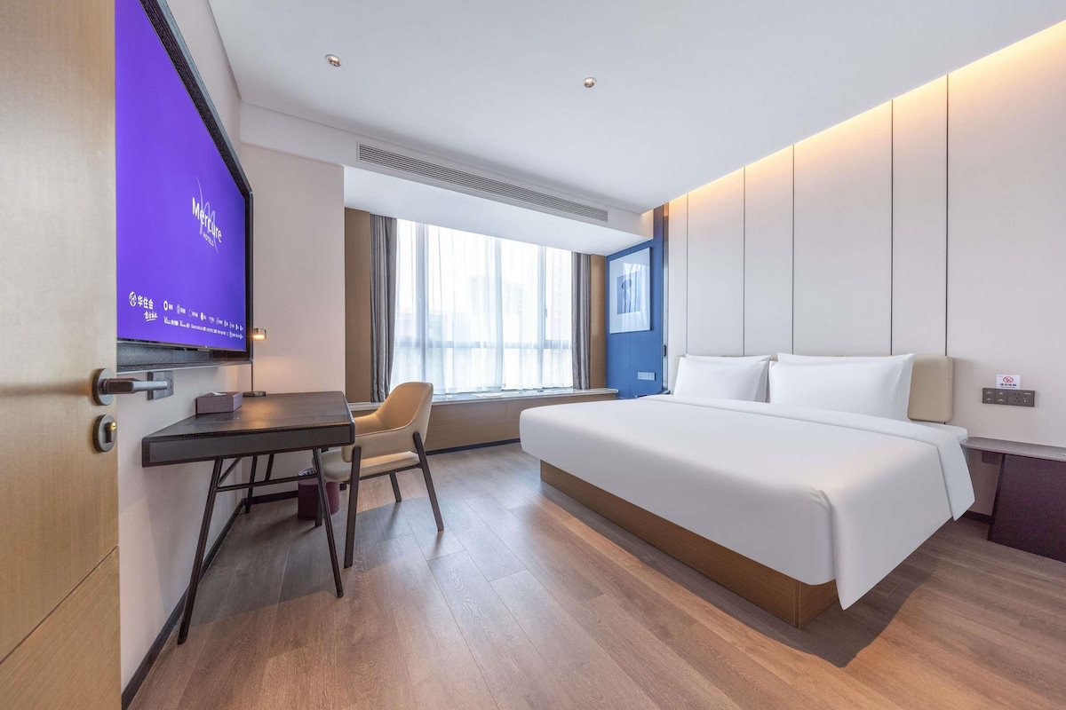 A hotel room with a bed, a desk, a chair, a television, and a window with curtains.