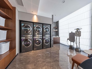 A modern laundry room with four wall-mounted washing machines, a small cabinet, and a seating area with a table.