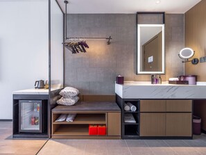 A modern bathroom with a large mirror, a towel rack, a sink with toiletries, and a small storage unit.