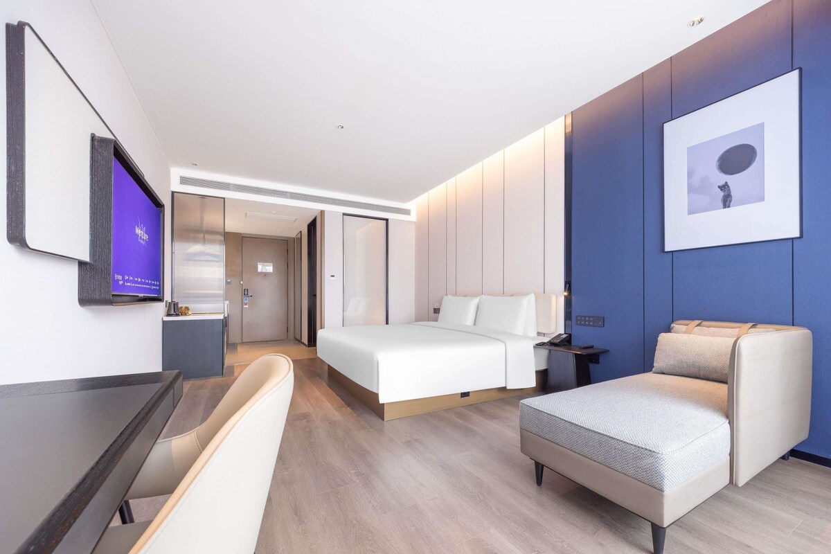 A modern hotel room with a bed, a desk, a chair, and a television.