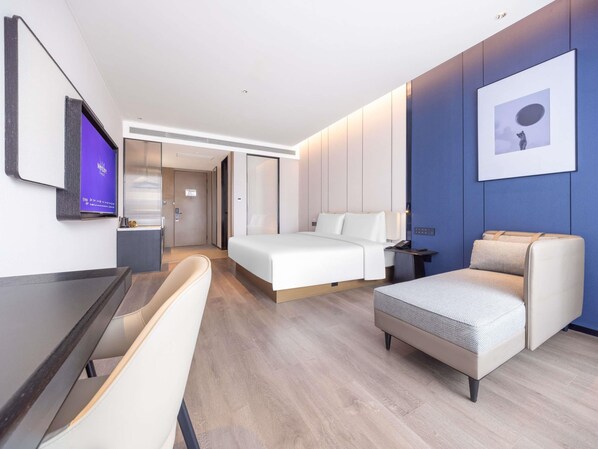 A modern hotel room with a bed, a desk, a chair, and a television.