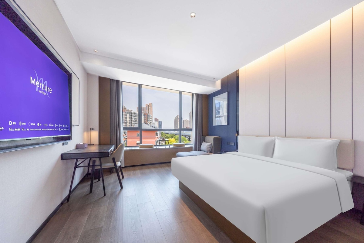 A hotel room with a large bed, a desk, a chair, and a TV mounted on the wall.