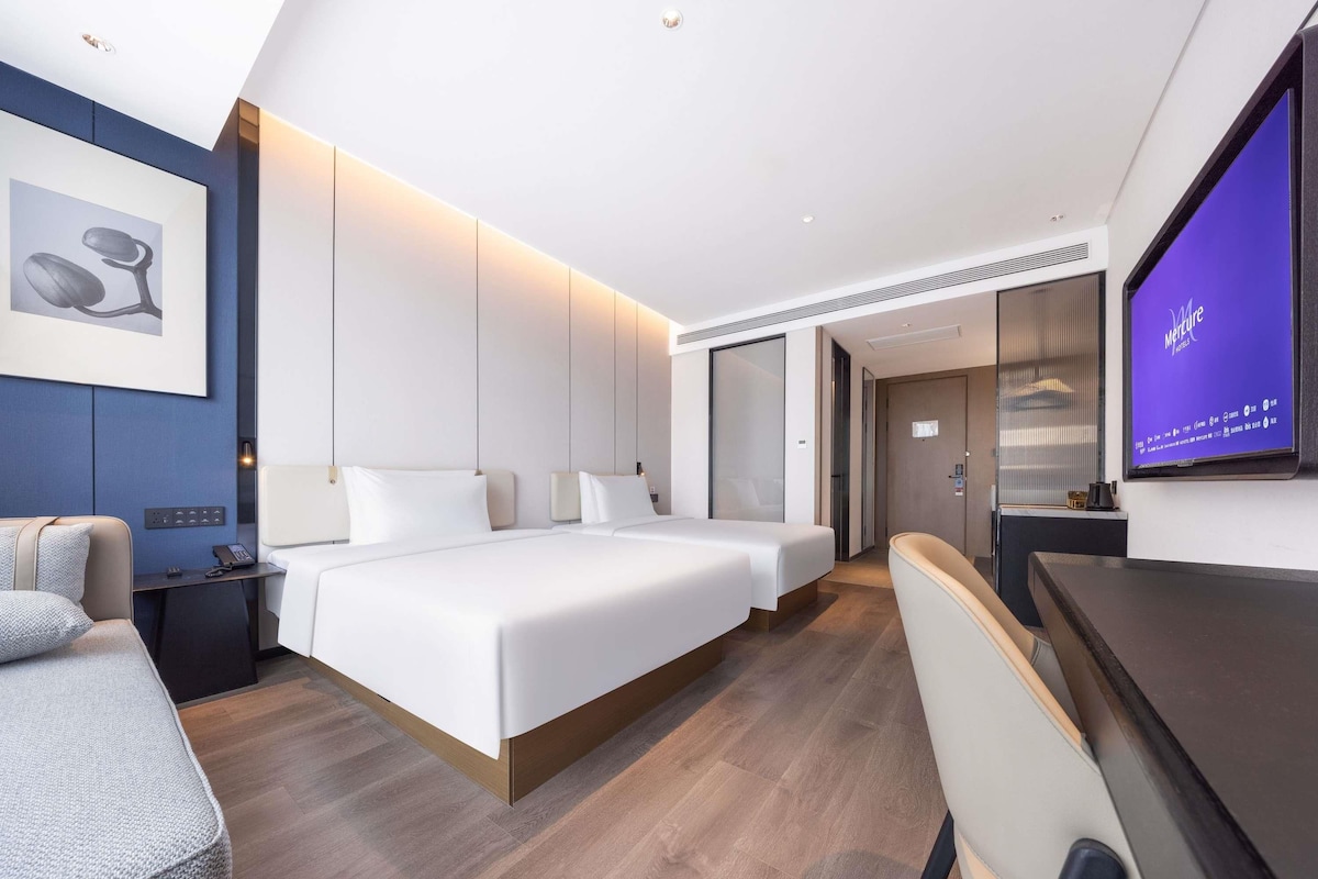 A modern hotel room with a large bed, bedside tables, a desk, and a television.
