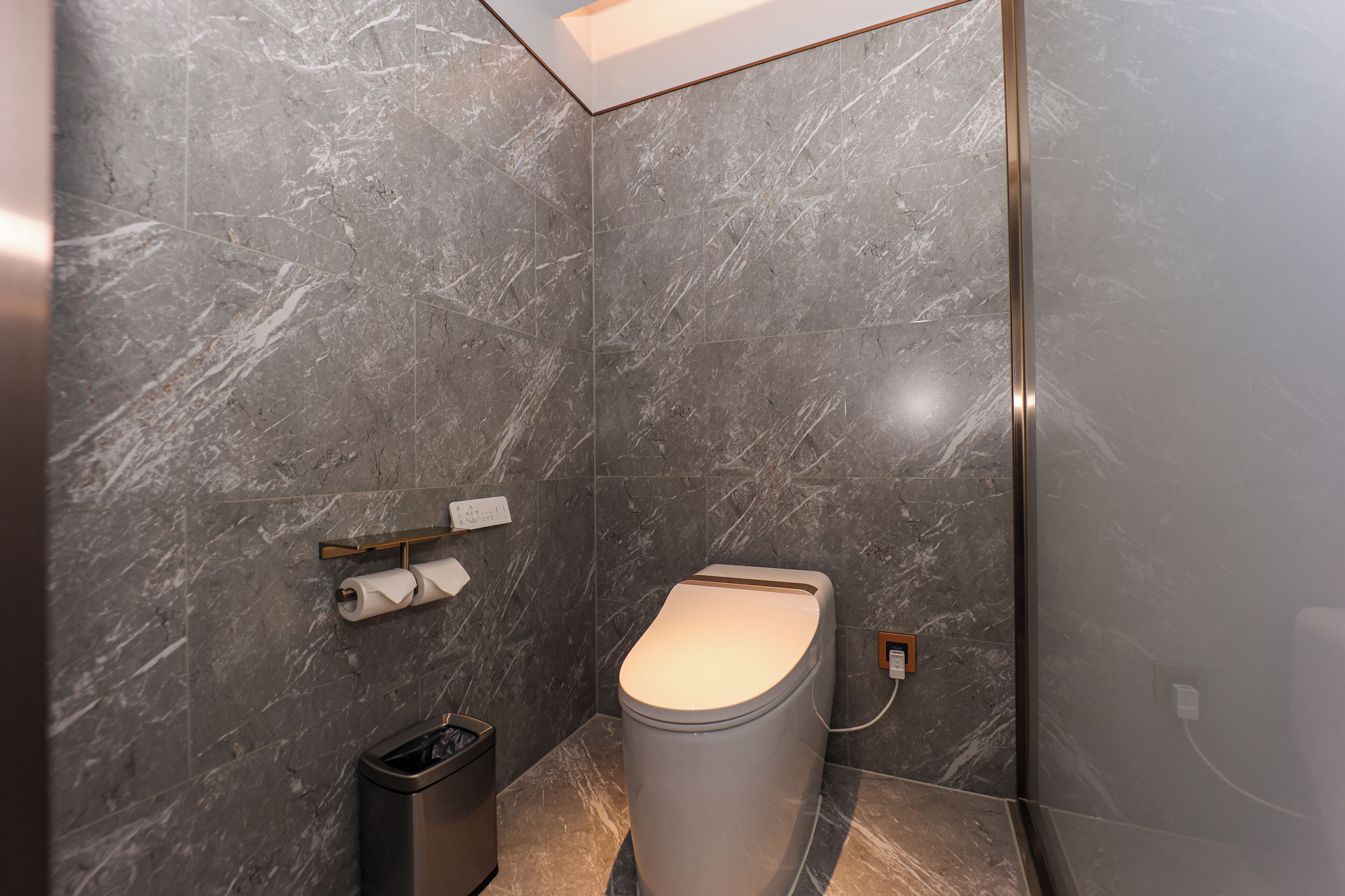 A modern bathroom with a toilet, a trash bin, and a towel holder on the wall.
