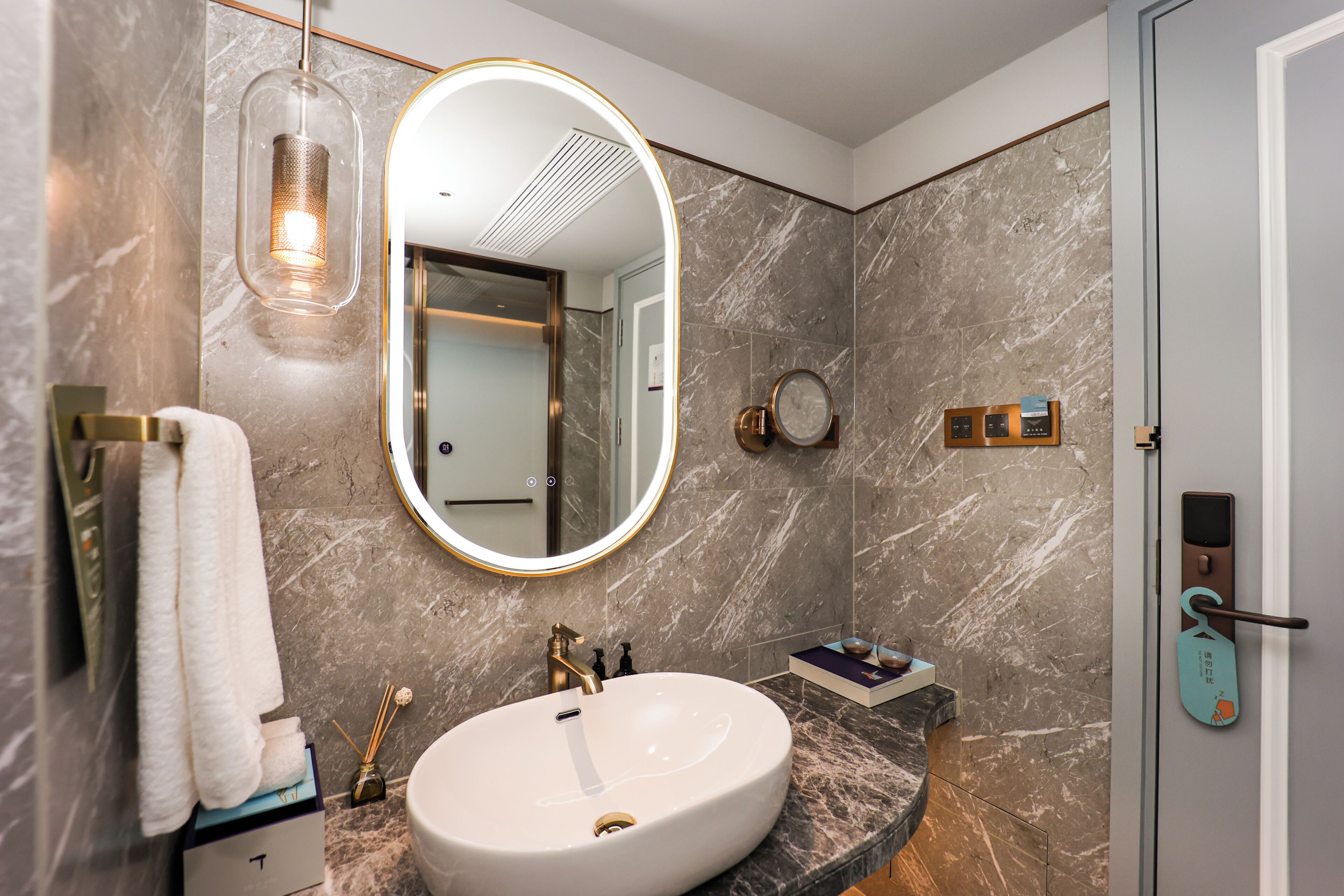 A bathroom with a marble sink, a large mirror, a towel rack, and a door with a keycard lock.