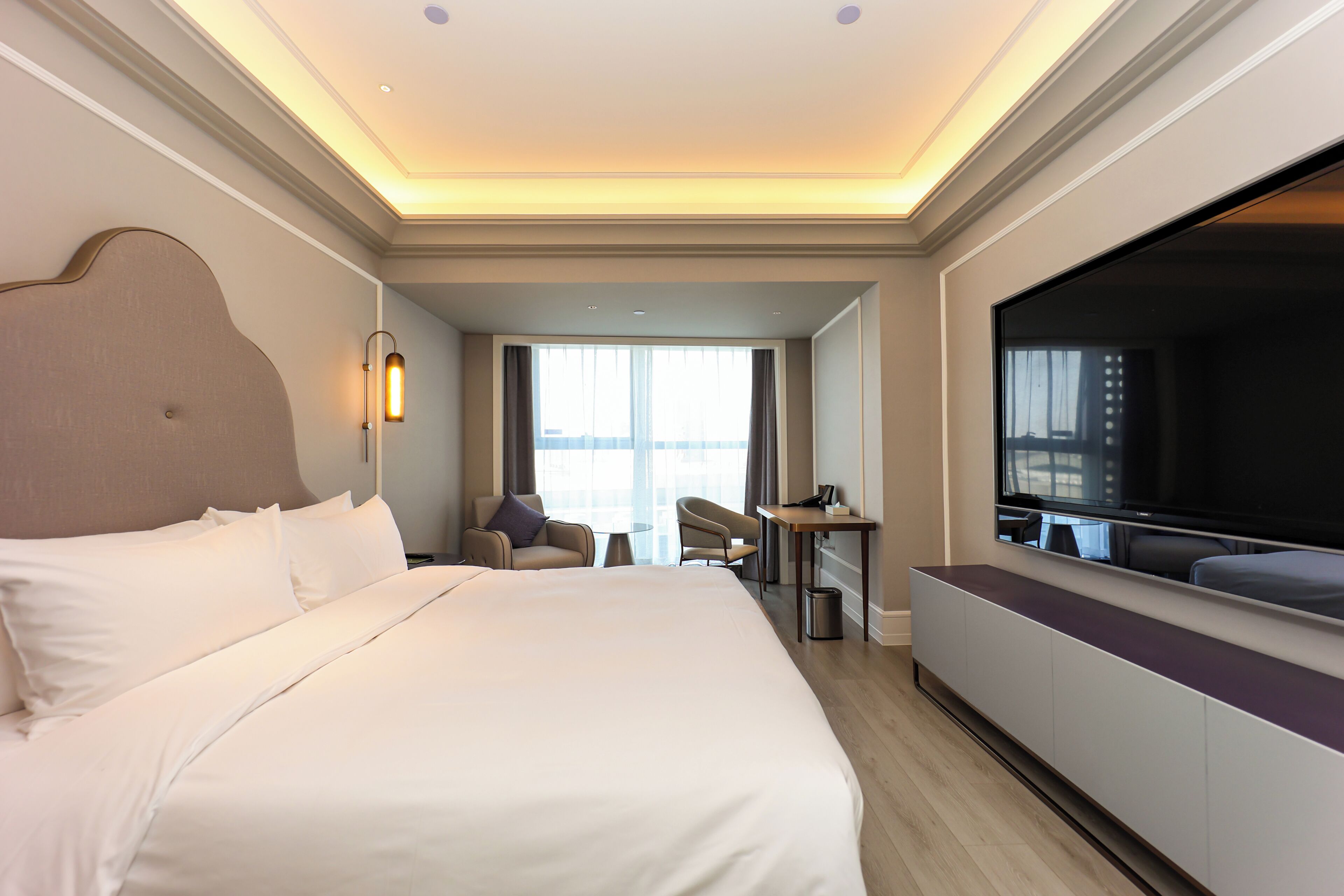A hotel room with a large bed, a TV, a desk, and a chair.