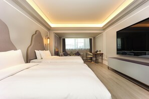 Habitació d'hotel amb dos llits, una escriptori, una cadira, un televisor i un finestral gran.