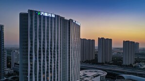 A high-rise building with vertical lines, a curved structure at the base, and multiple smaller buildings in the background. - Mercure Jinan West Railway Station (Jinan)