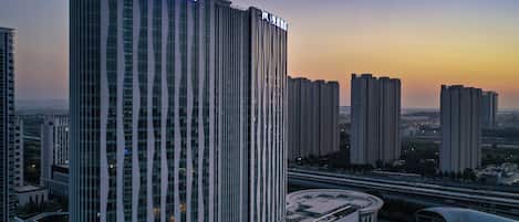 Un edificio alto de líneas verticales, una estructura curva en la base y varios edificios más pequeños al fondo.