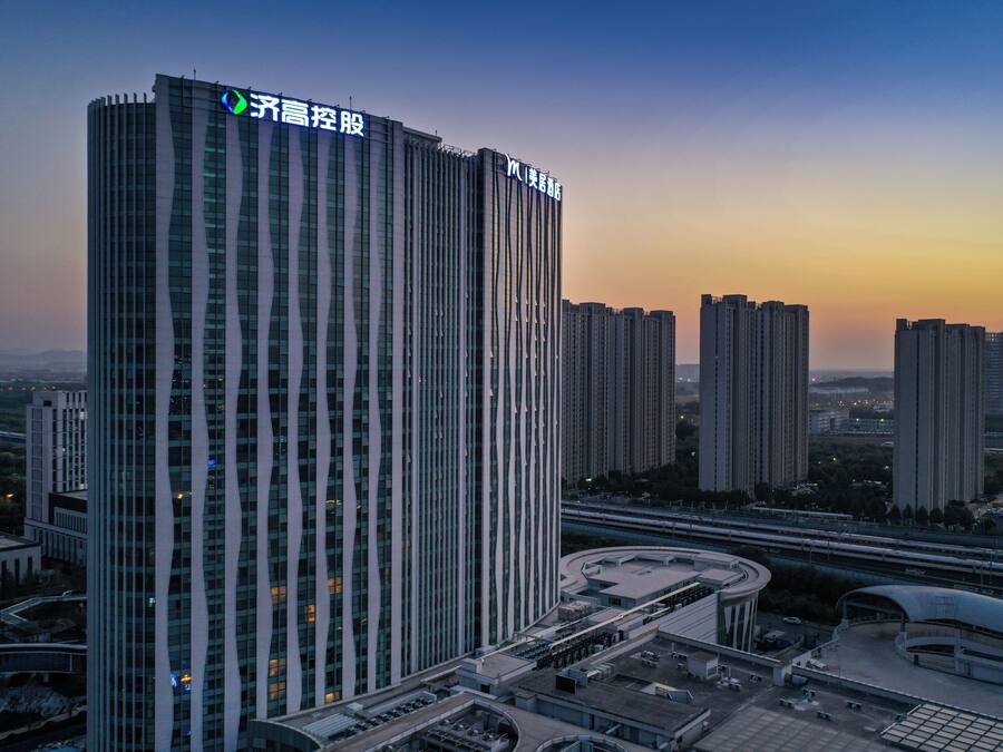 A high-rise building with vertical lines, a curved structure at the base, and multiple smaller buildings in the background.