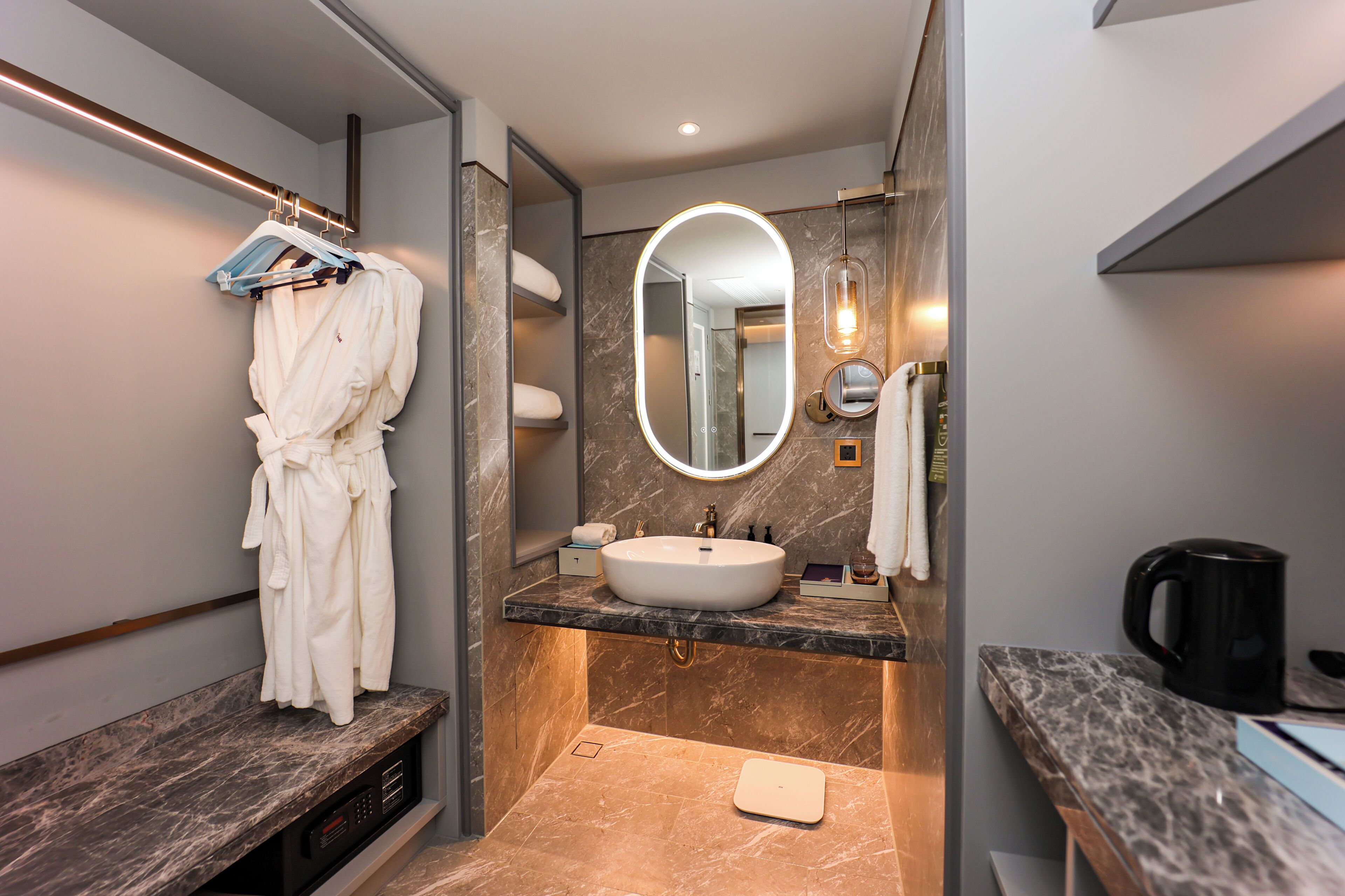 A modern bathroom with a marble sink, a large mirror, a robe rack, and a coffee maker.