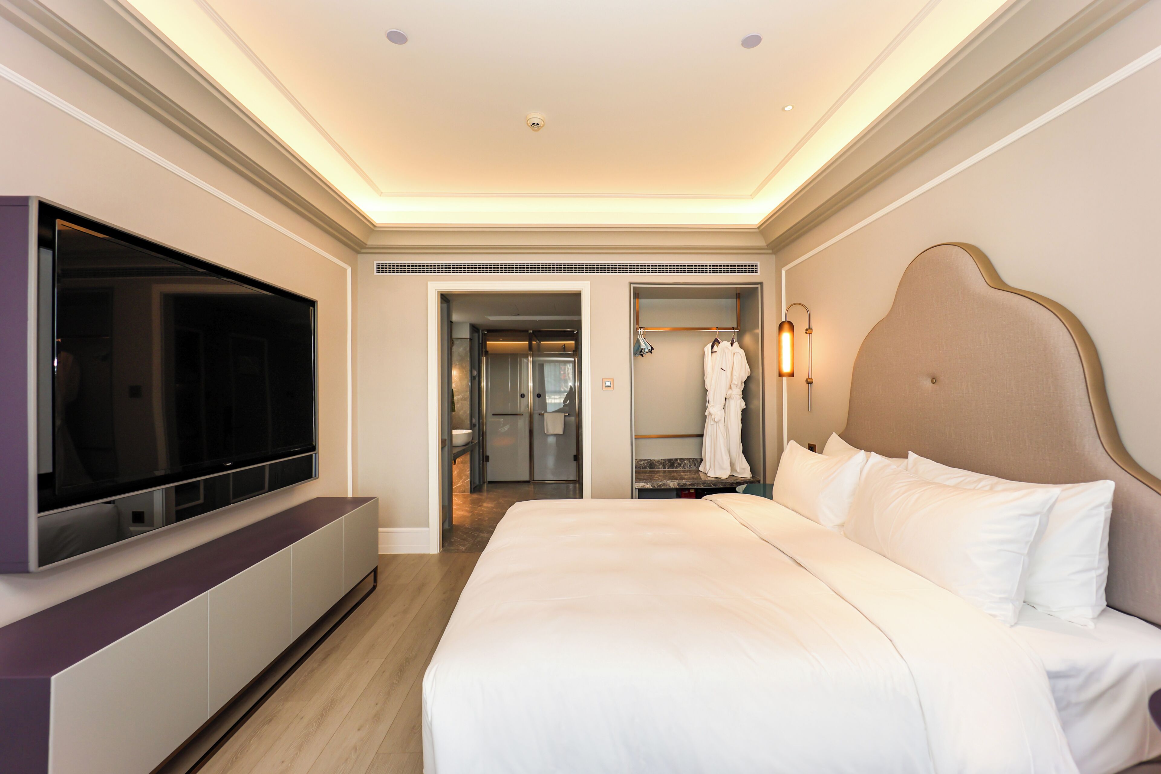 Une chambre d’hôtel avec un grand lit, une télévision à écran plat, un dressing et une salle de bain.