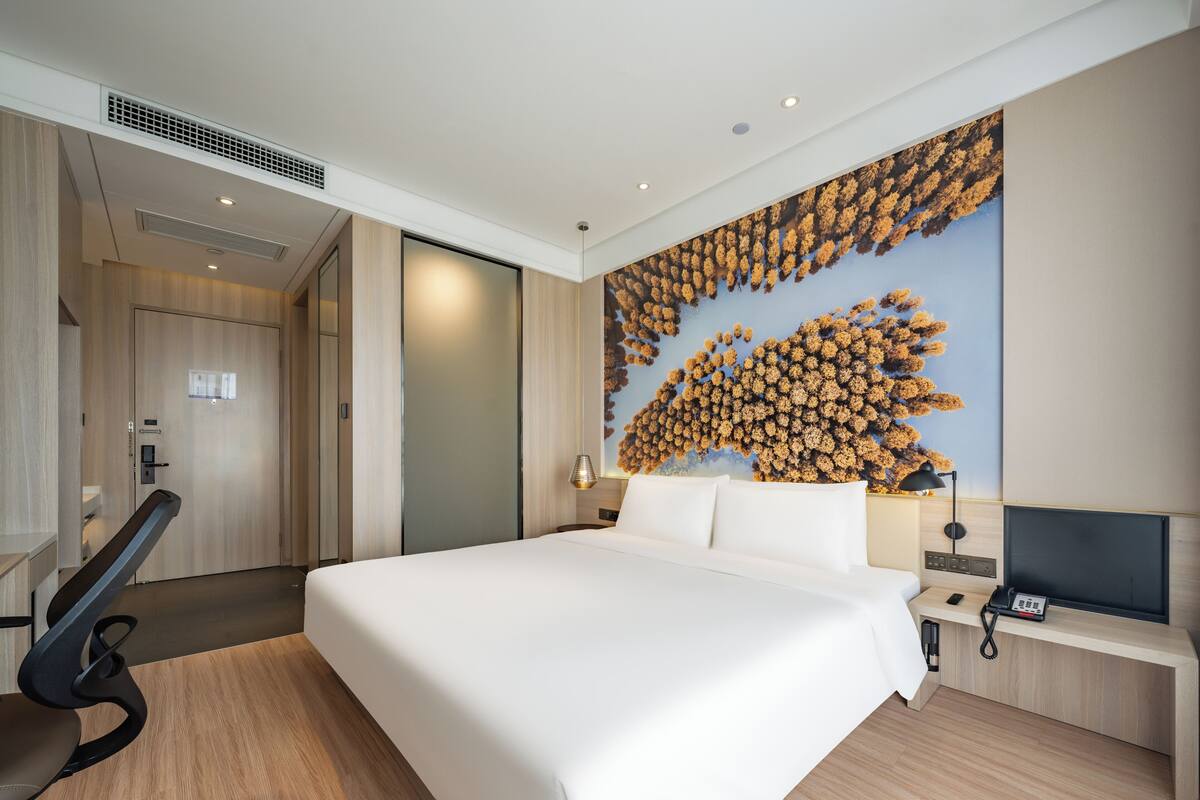 A modern hotel room with a large bed, a desk with a phone, a chair, and a wall with a textured design.