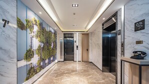 A modern hotel lobby with a marble floor, a reception desk, an elevator, and a wall with a cityscape mural. - Mercure Shanghai Pudong Zhangjiang Park (Shanghai)