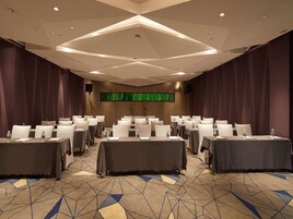 A conference room with tables and chairs, a patterned carpet, and a large screen on the wall.