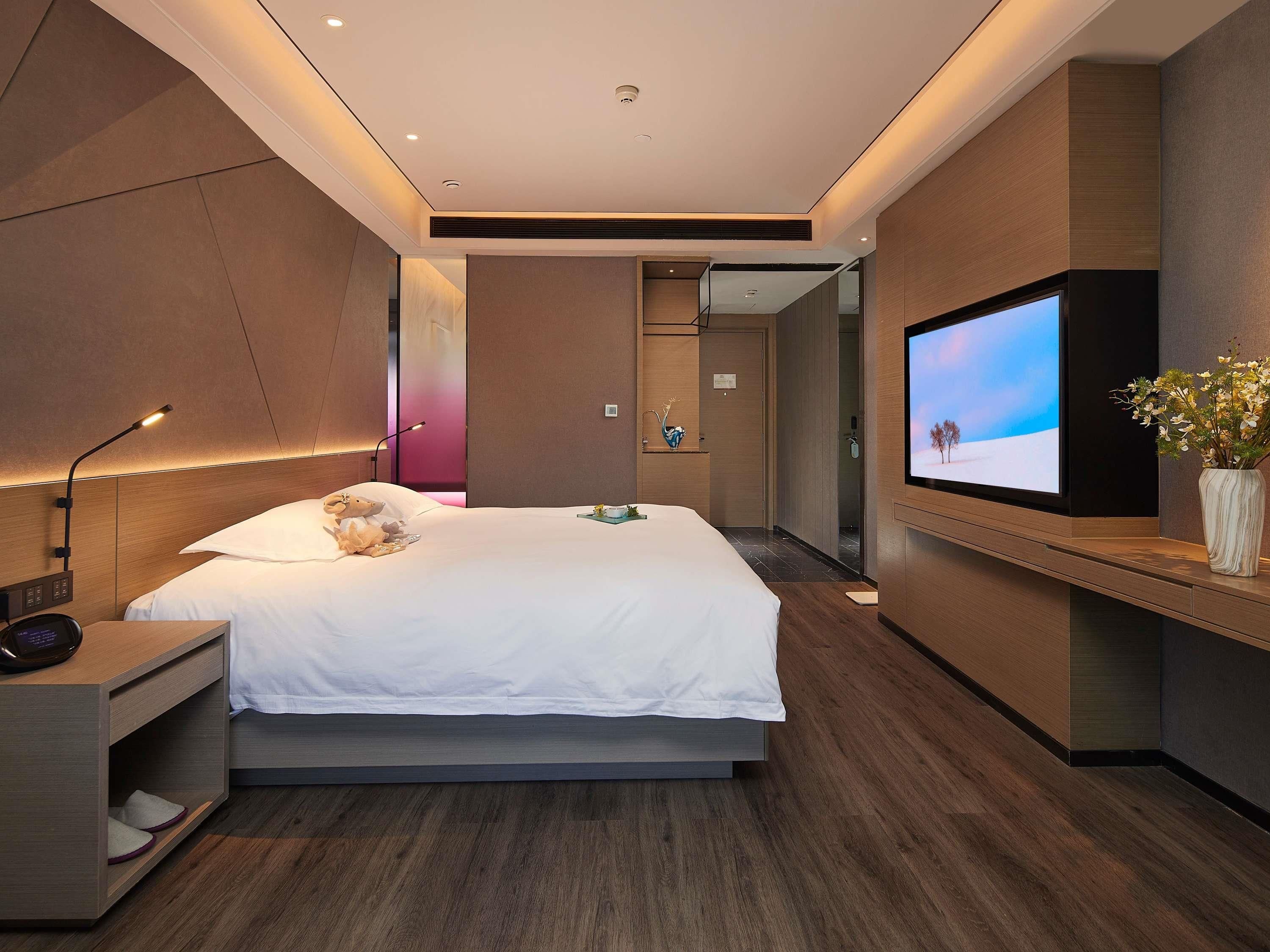 Habitació d'hotel moderna amb un llit gran, una televisió, una taula de nit i un taulell.