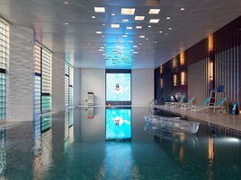 Una piscina interior moderna con agua cristalina, una pantalla digital y sillones de descanso.