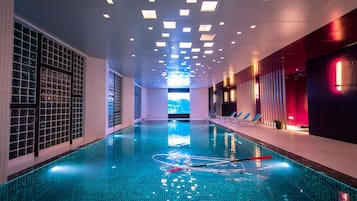 An indoor swimming pool with clear water, tiled walls, and ceiling lights.