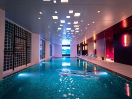 An indoor swimming pool with clear water, tiled walls, and ceiling lights.