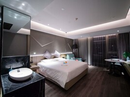 A modern hotel room with a large bed, a bedside table, a round mirror, and a bathroom with a marble sink.